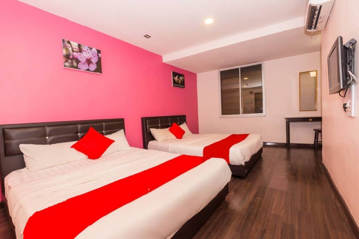 Een hotelkamer met twee bedden, roze muren en een raam.