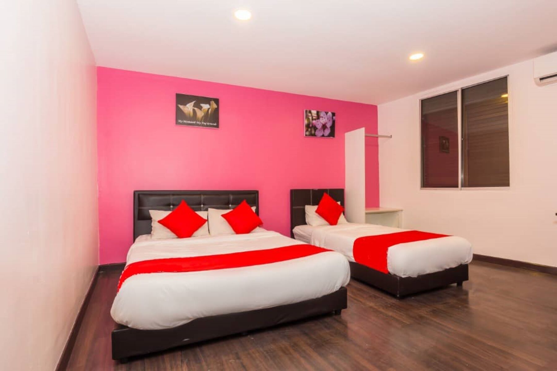 A hotel room with two beds, pink walls, and wooden flooring.