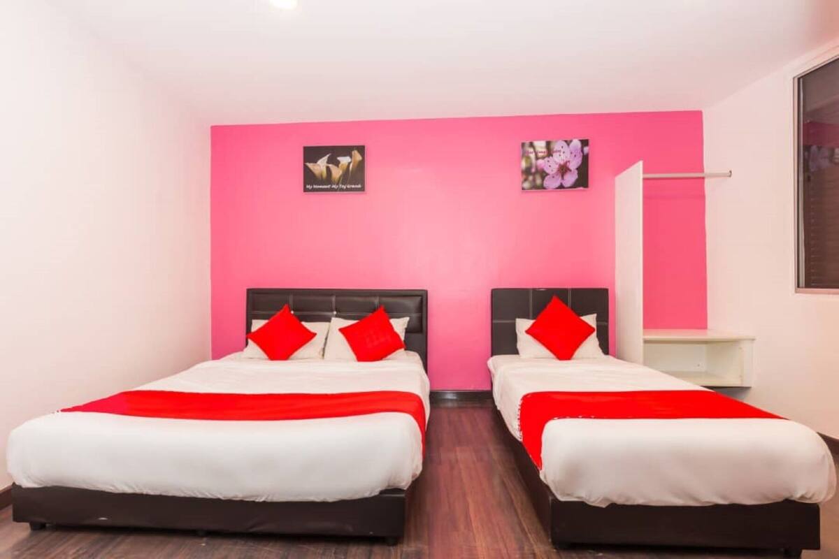 Een hotelkamer met twee bedden, elk voorzien van witte beddengoed en rode accenten, tegen een roze muur.