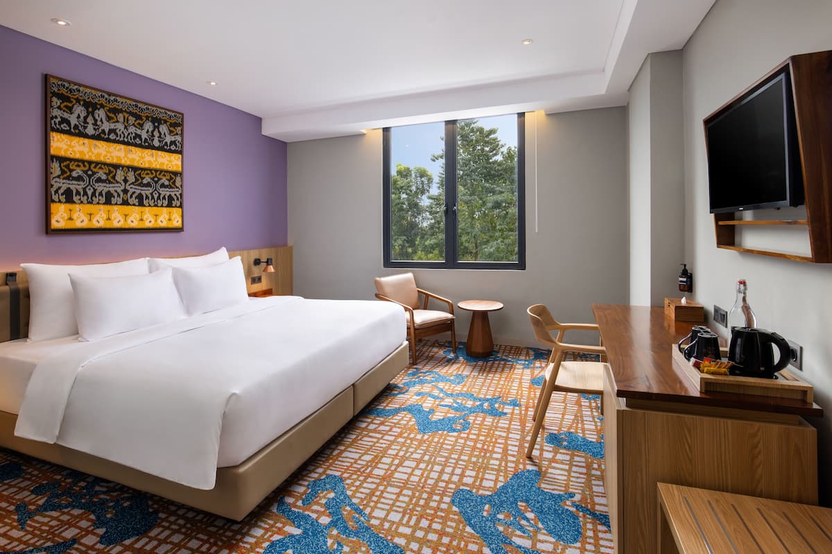 Een moderne hotelkamer met een groot bed, een bureau met koffiezetapparaat, een televisie en een raam met uitzicht op bomen.