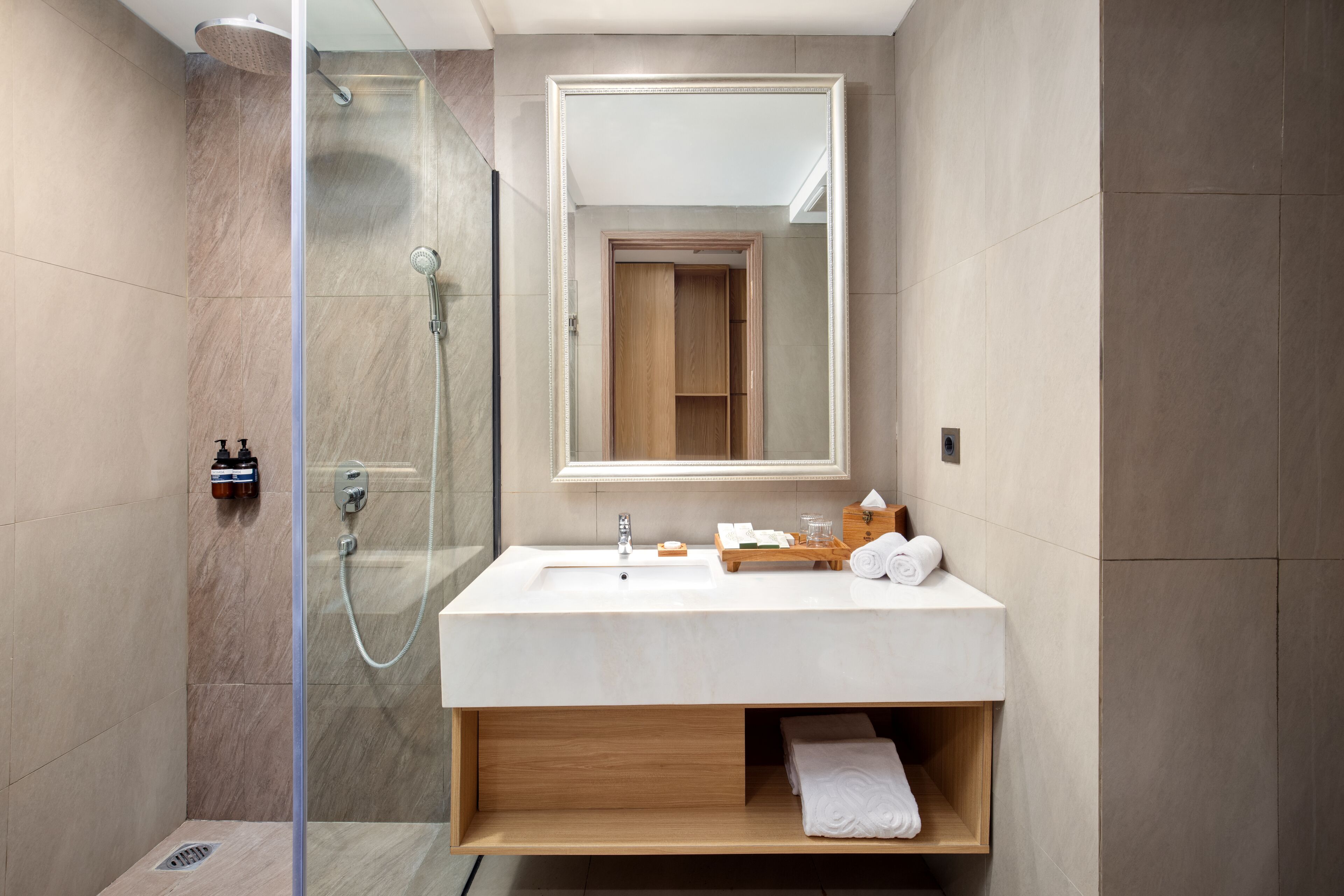 A modern bathroom with a glass-enclosed shower, a large mirror, a sink with toiletries, and a wooden vanity.