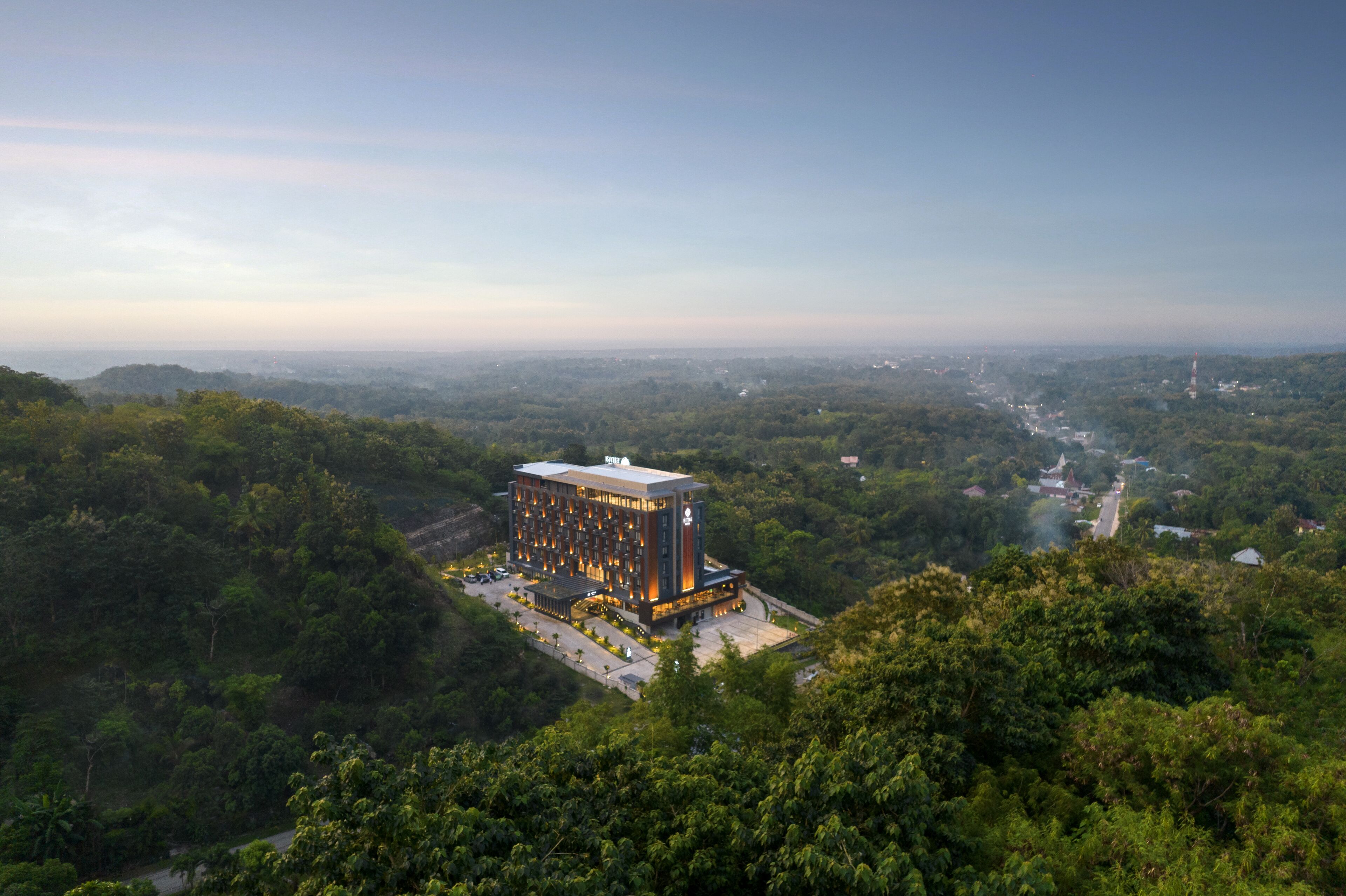 Un hotel moderno con techo plano, rodeado de vegetación exuberante y cielo despejado.
