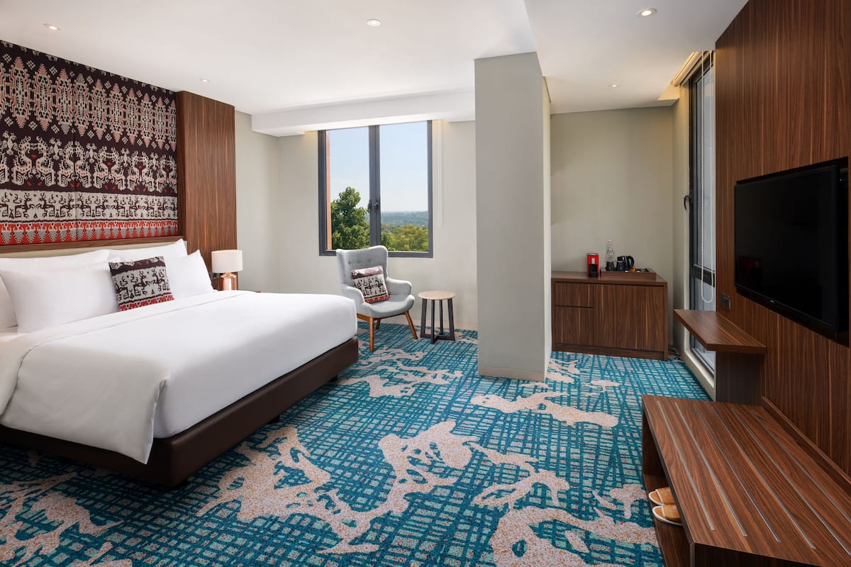 Een moderne hotelkamer met een groot bed, een televisie, een klein tafeltje en een stoel.