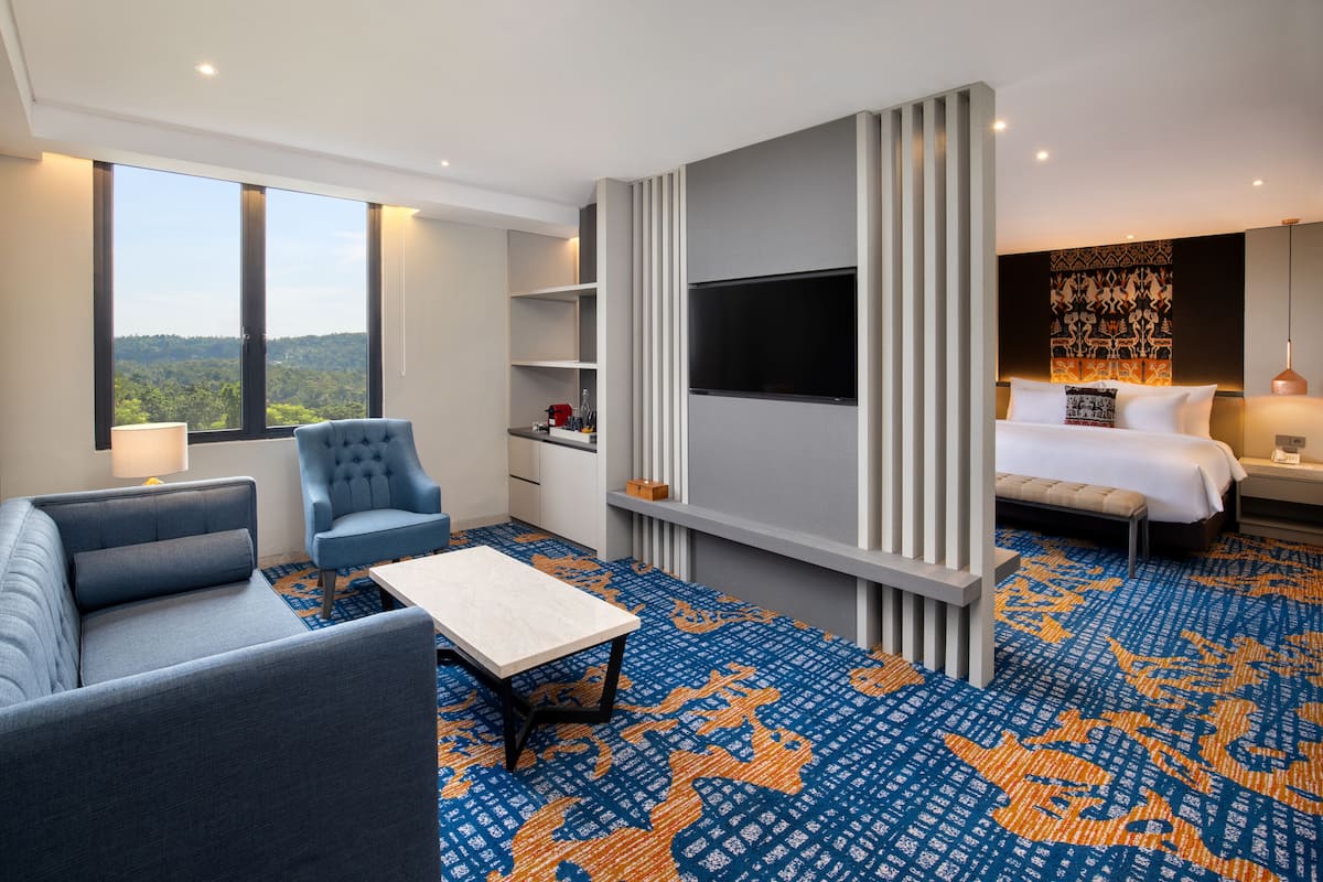 Een hotelkamer met een groot raam, een bank, een televisie, een bed en een kamerbreed tapijt met een patroon.