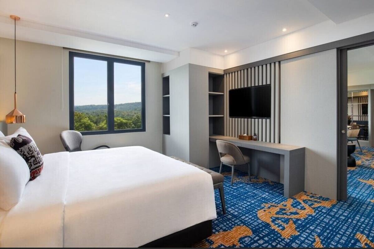 Een hotelkamer met een groot bed, een bureau, een flatscreen televisie, een stoel en uitzicht op het omliggende landschap.