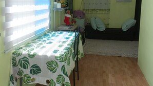 En kompakt opholdsstue med spisebord, sofa, loftventilator og et vindue med persienner.