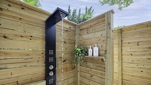A wooden outdoor shower enclosure with a black showerhead, two bottles of Native body wash, and a potted plant. - Pet friendly beach house w/private backyard & outdoor shower- steps from beach (St. Augustine)