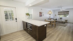A modern kitchen with a built-in microwave, a dining area with a round table and chairs, and a living room with a sofa and a coffee table. - Pet friendly beach house w/private backyard & outdoor shower- steps from beach (St. Augustine)