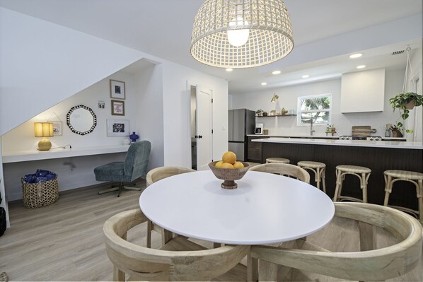 Una cocina moderna con una isla central, un comedor con una mesa redonda y sillas, y una lámpara colgante.
