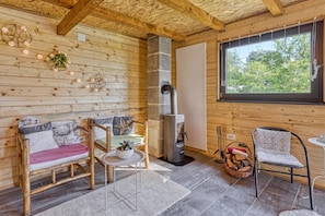 Ein gemütliches Blockhaus-Interieur mit Holzausbau, einer Couch, einem Sessel, einem Tisch, einem Fenster und einem Holzofen.