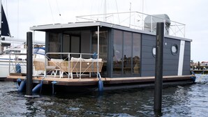 Ein schwimmendes Hausboot mit überdachter Terrasse, Sitzgelegenheit und Fenstern.