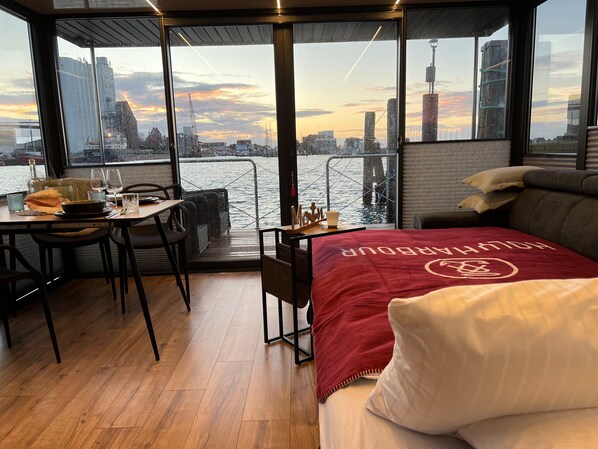 A room with a view of a cityscape, a dining area with chairs and a table, and a bed with a red blanket.