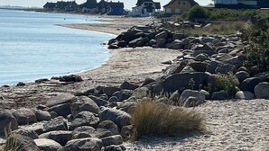 Ein Küstenstrand mit felsigem Ufer, einem Sandstrand und Häusern im Hintergrund.