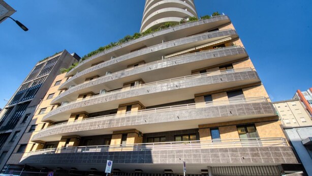 A multi-story building with balconies, a cylindrical tower, and a clear sky. - GuestHost - Cherenel House (Milan)
