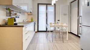 A modern kitchen with white cabinets, a dining table with chairs, and a refrigerator. - GuestHost - Cherenel House (Milan)