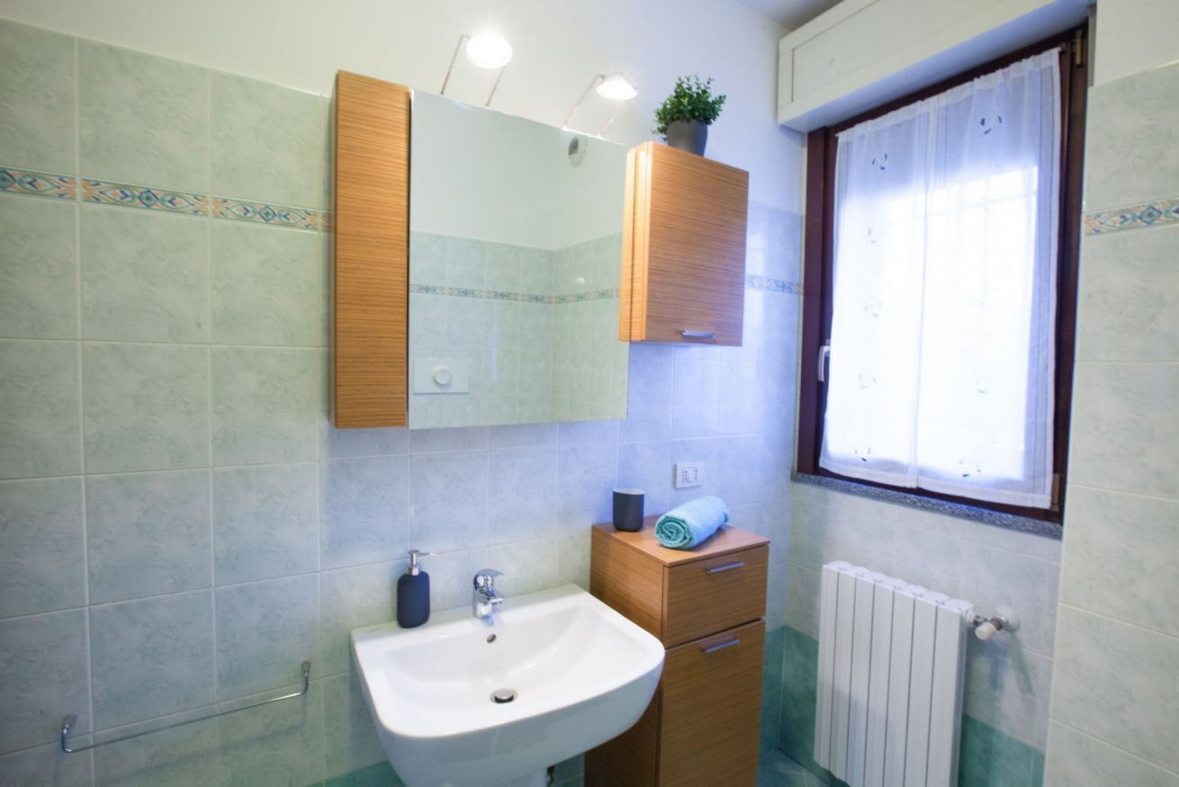 A bathroom with a sink, mirror, cabinet, and window.