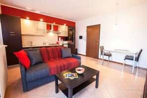 A modern living room with a sofa, coffee table, and a dining area with chairs and a table. - GuestHost - The Gardens (Vimodrone)