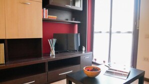 A modern living room with dark wooden furniture, a flat-screen TV, a bowl on a table, and a view through a glass door. - GuestHost - The Gardens (Vimodrone)