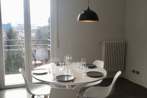 A dining area with a round table, white chairs, and a black pendant light. - GuestHost - CASA LUMIÈRE (Cernusco sul Naviglio)