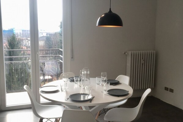 A dining area with a round table, white chairs, and a black pendant light.