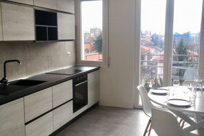 A modern kitchen with a large window, a dining table with chairs, and a view of buildings outside.