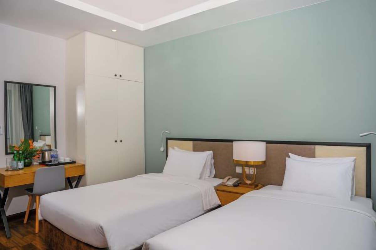 A hotel room with two beds, a desk, a chair, a mirror, and a lamp.