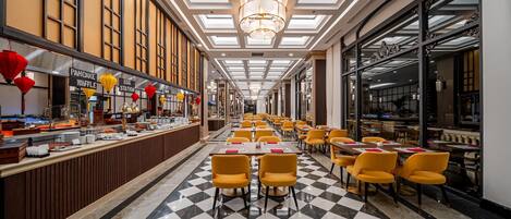 A spacious hotel lobby with a checkered floor, yellow chairs, a long reception desk, and a modern chandelier.