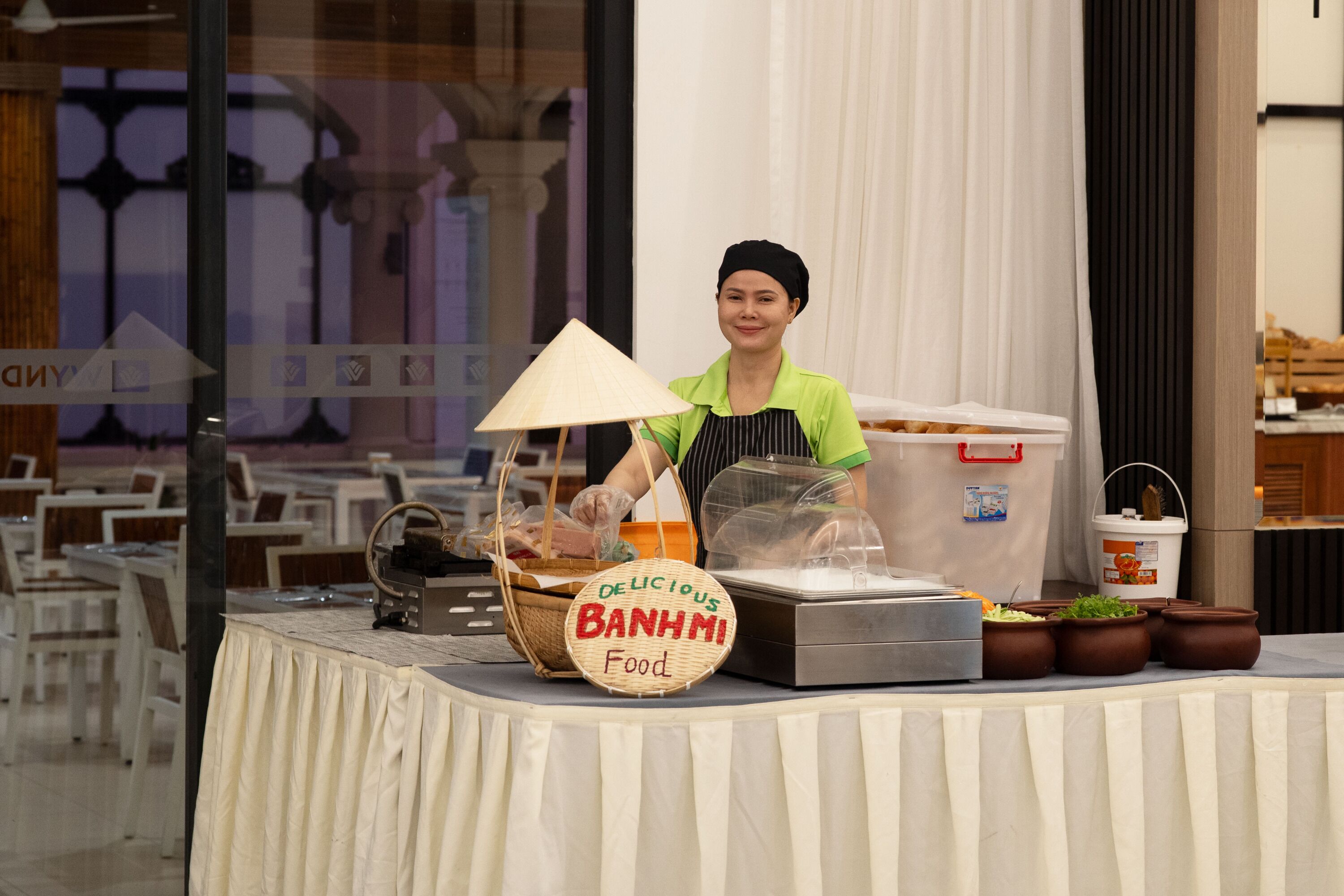 A buffet setup with a sign reading "DELICIOUS BANHMI Food" and various dishes displayed.