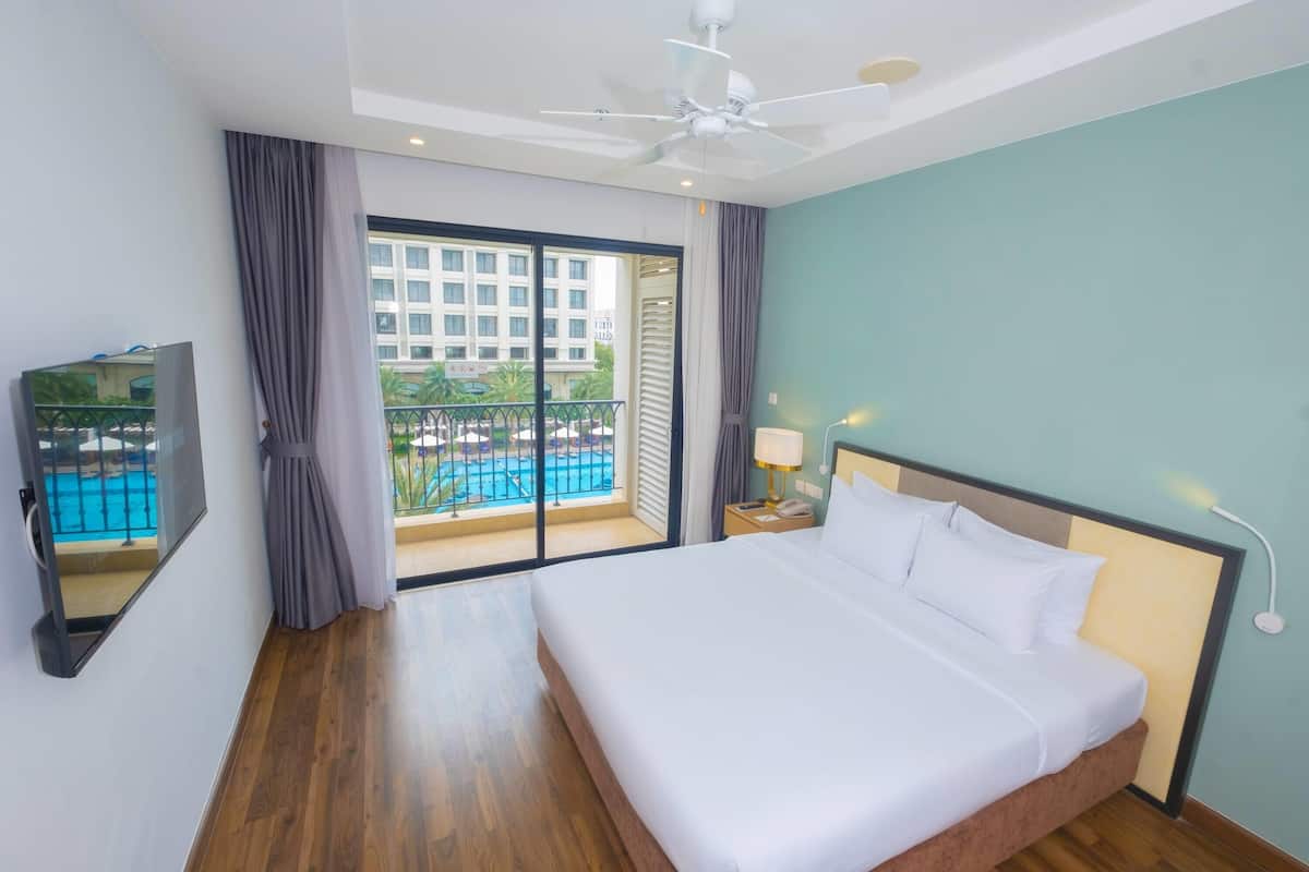 Habitación de hotel con una cama grande, un ventilador de techo, un televisor y vista a una piscina.