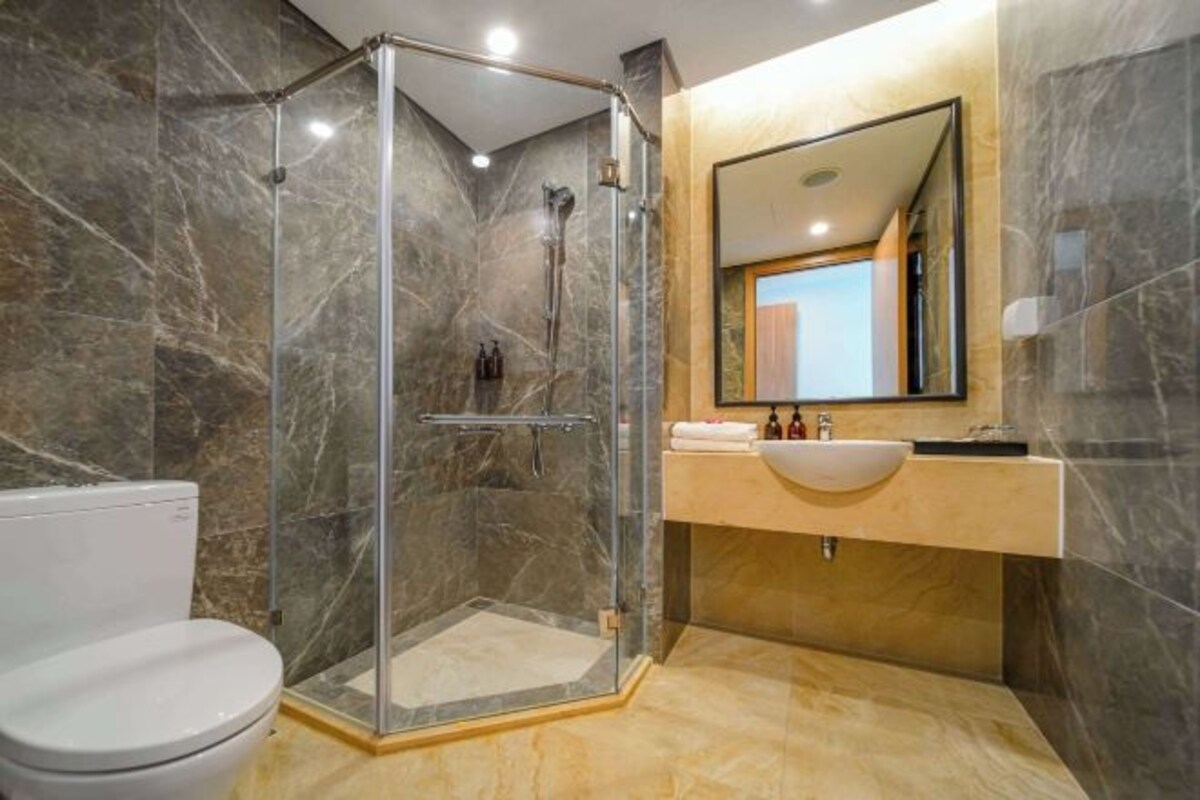 Une salle de bain moderne avec une douche à parois de verre, des toilettes blanches et un meuble-lavabo doté d’un miroir et d’un évier.