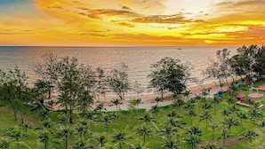 A coastal landscape with a beach, palm trees, and a sunset.