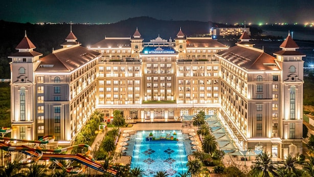 A large, well-lit hotel with a central courtyard pool, multiple wings, and a mountainous backdrop.