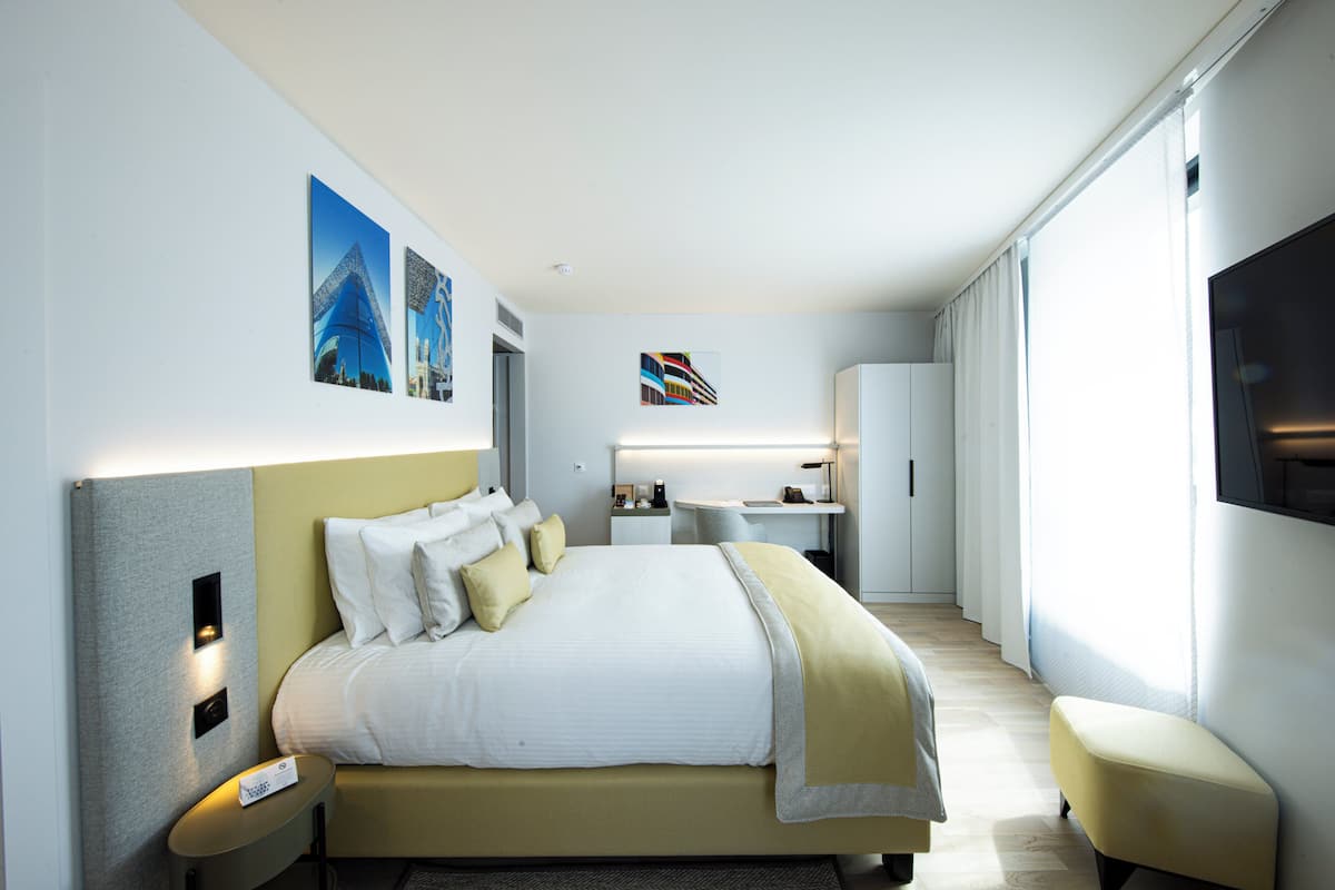 A modern hotel room with a large bed, bedside tables, a desk, and a TV.