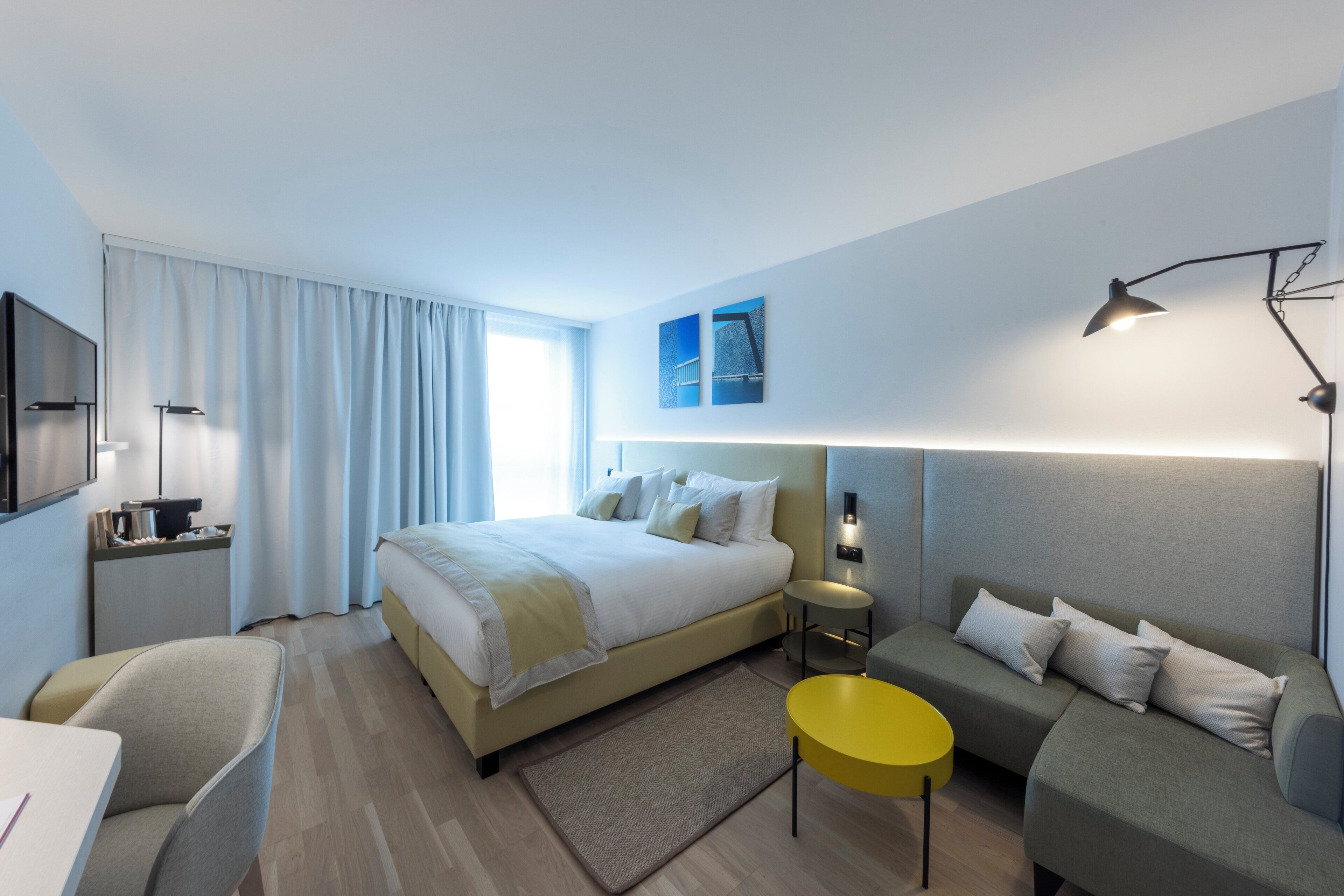 Een moderne hotelkamer met een bed, een bank, een tafeltje en een televisie.