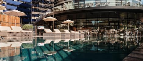 A modern hotel with a pool area, lounge chairs, and umbrellas.
