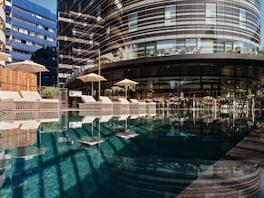 A modern hotel with a pool area, lounge chairs, and umbrellas. - Crowne Plaza Marseille Le Dome by IHG (Marseille)