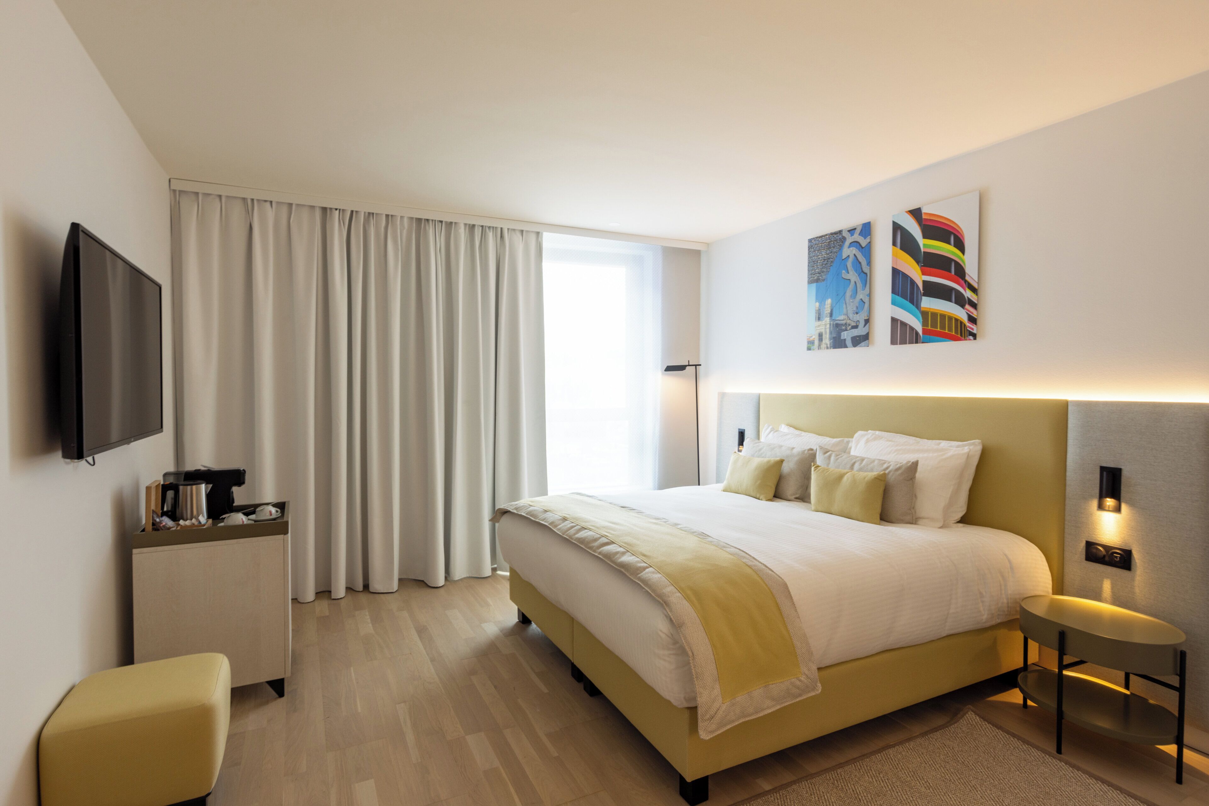 Una habitación de hotel con cama, escritorio, televisor y obras de arte en la pared.
