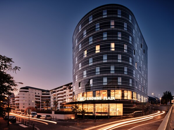 Ein modernes Hotel mit geschwungener Fassade, mehreren Etagen und einem markanten Eingang mit beleuchteter Beschilderung.