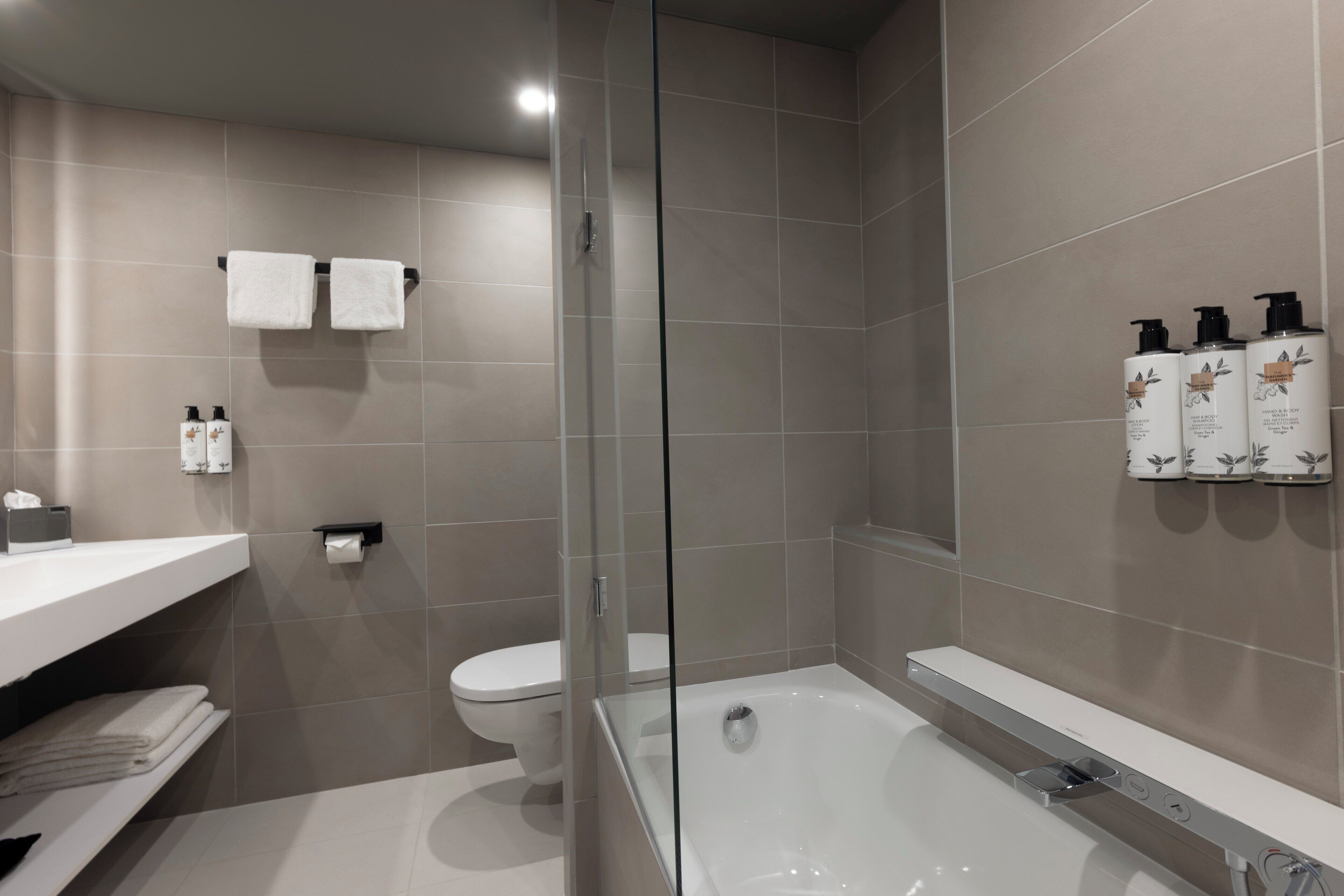 A modern bathroom with a glass-enclosed shower, a bathtub, and a toilet. There are towels and toiletries on the counter.