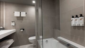 A modern bathroom with a glass-enclosed shower, a bathtub, and a toilet. There are towels and toiletries on the counter.