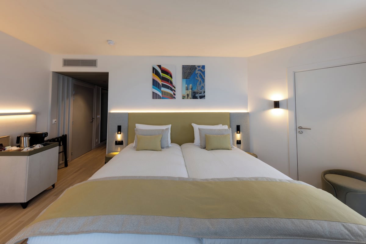 A hotel room with a double bed, two bedside tables, a desk with a chair, and a door.
