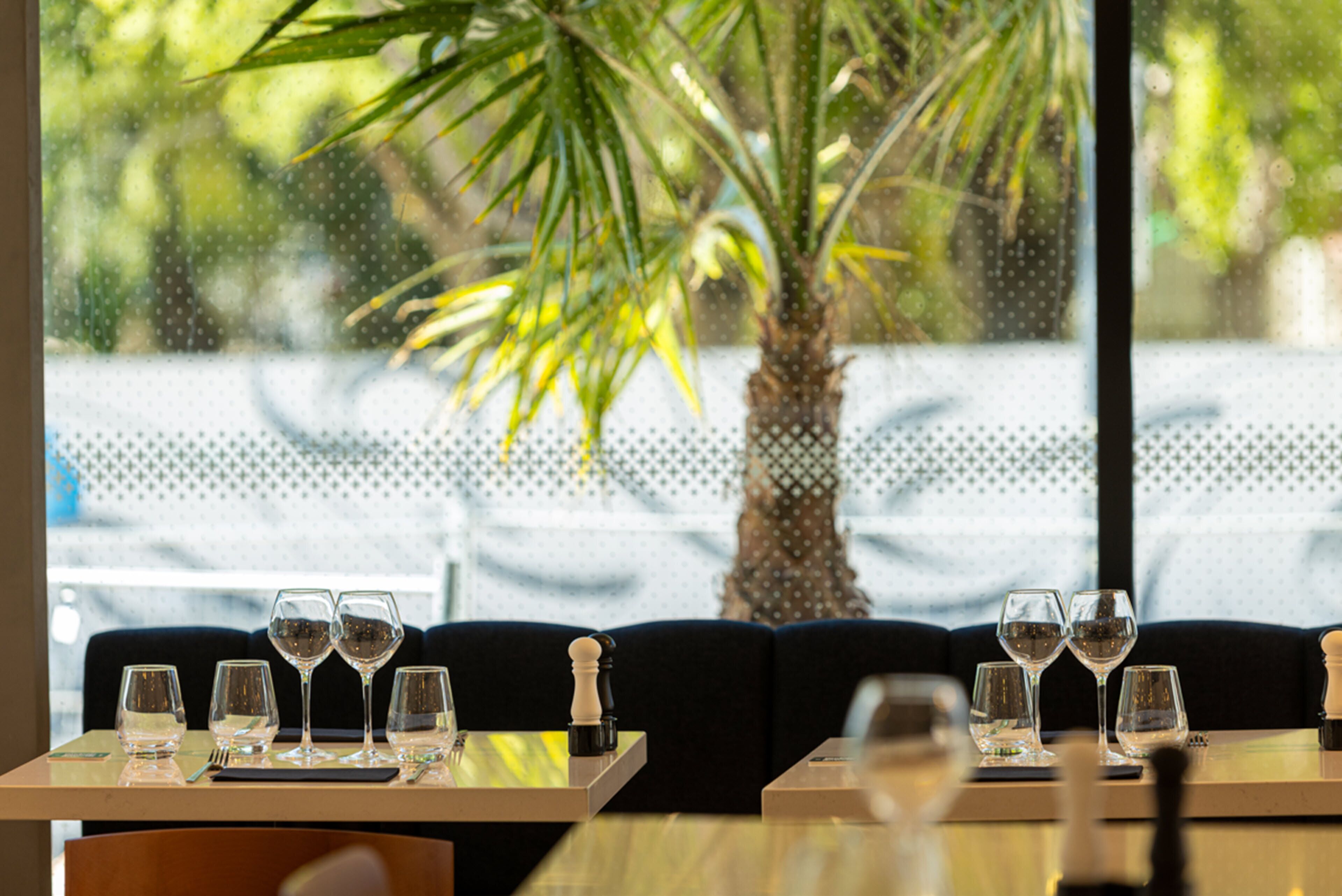 A restaurant table with empty wine glasses and cutlery, a chess piece, and a potted plant in the background.