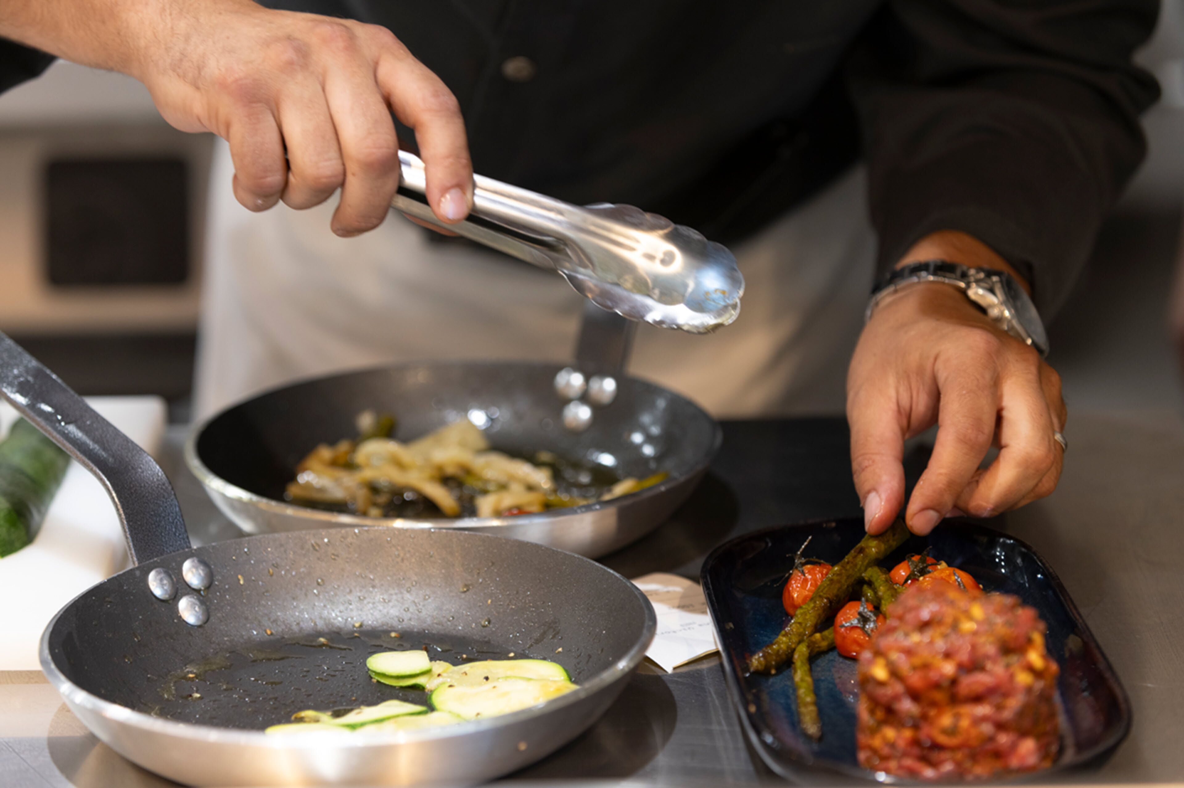A person cooking with tongs, a frying pan, and a plate with food.