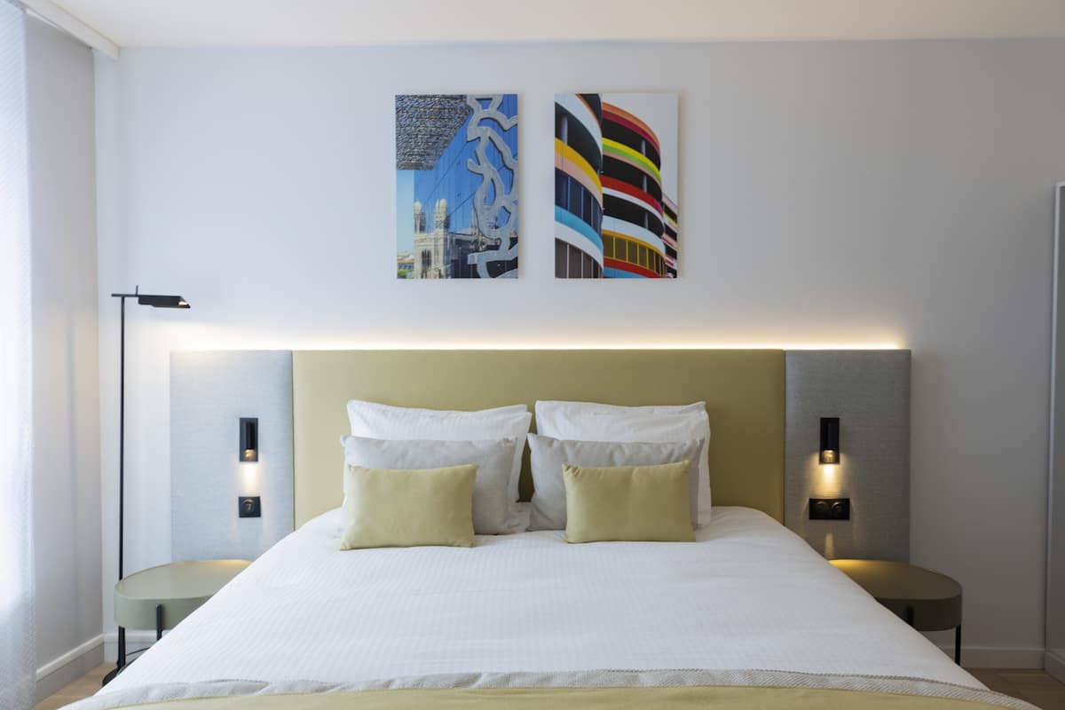 A modern hotel room with a large bed, two bedside tables, and wall-mounted lighting.