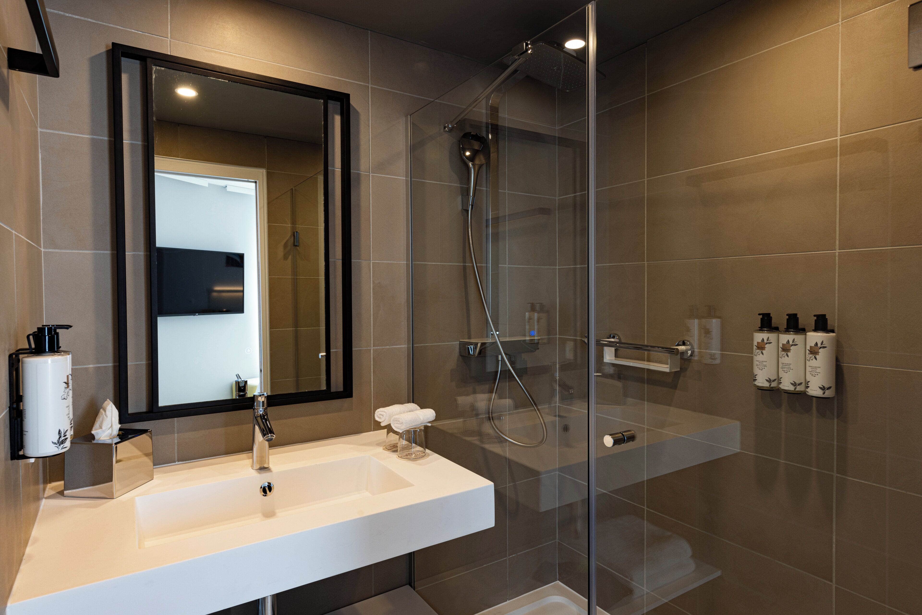 Un baño moderno con ducha envuelta en vidrio, un espejo grande y un lavabo blanco.