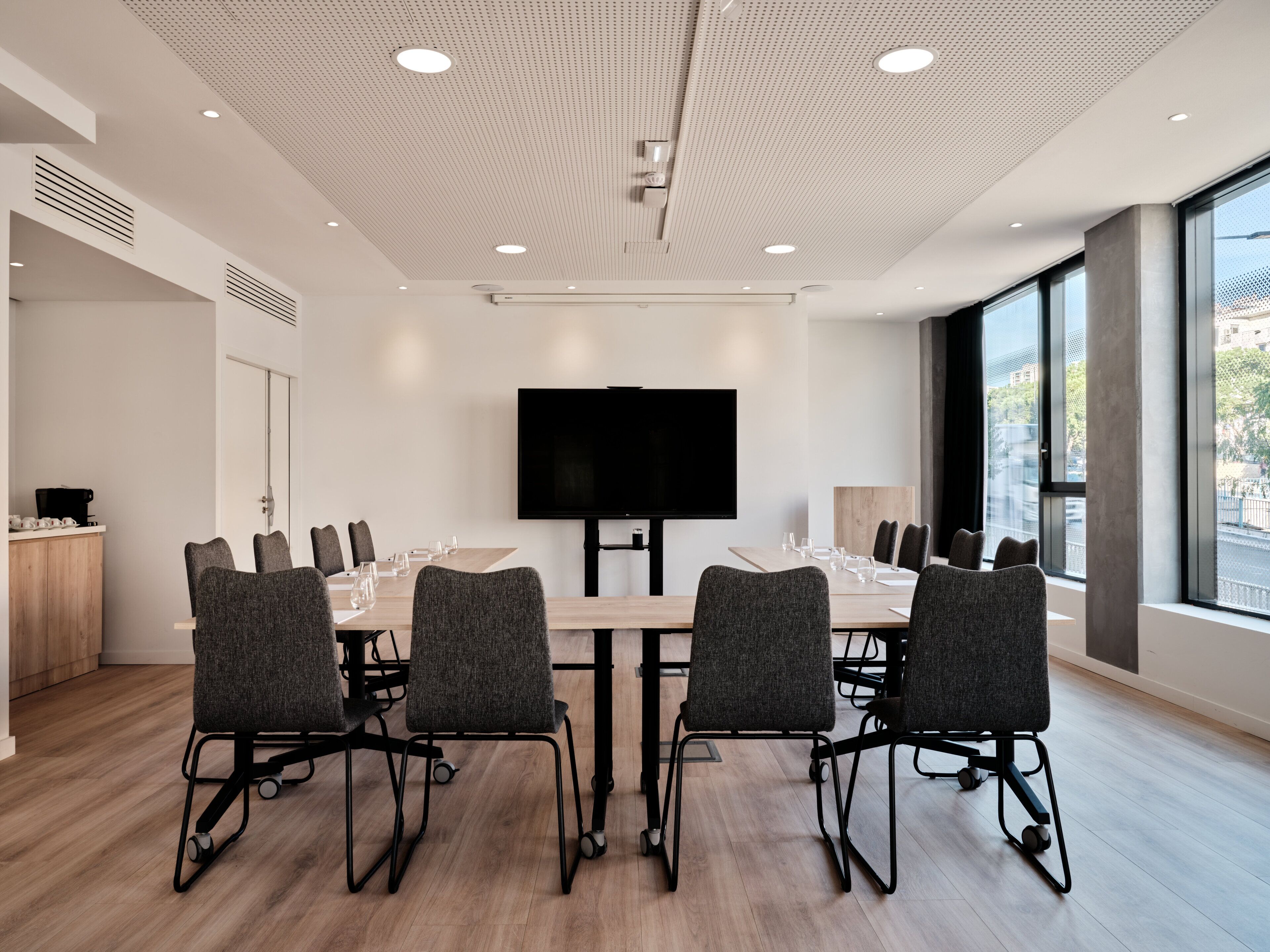 Una sala conferenze con un grande schermo piatto, sedie moderne e un tavolo in legno.