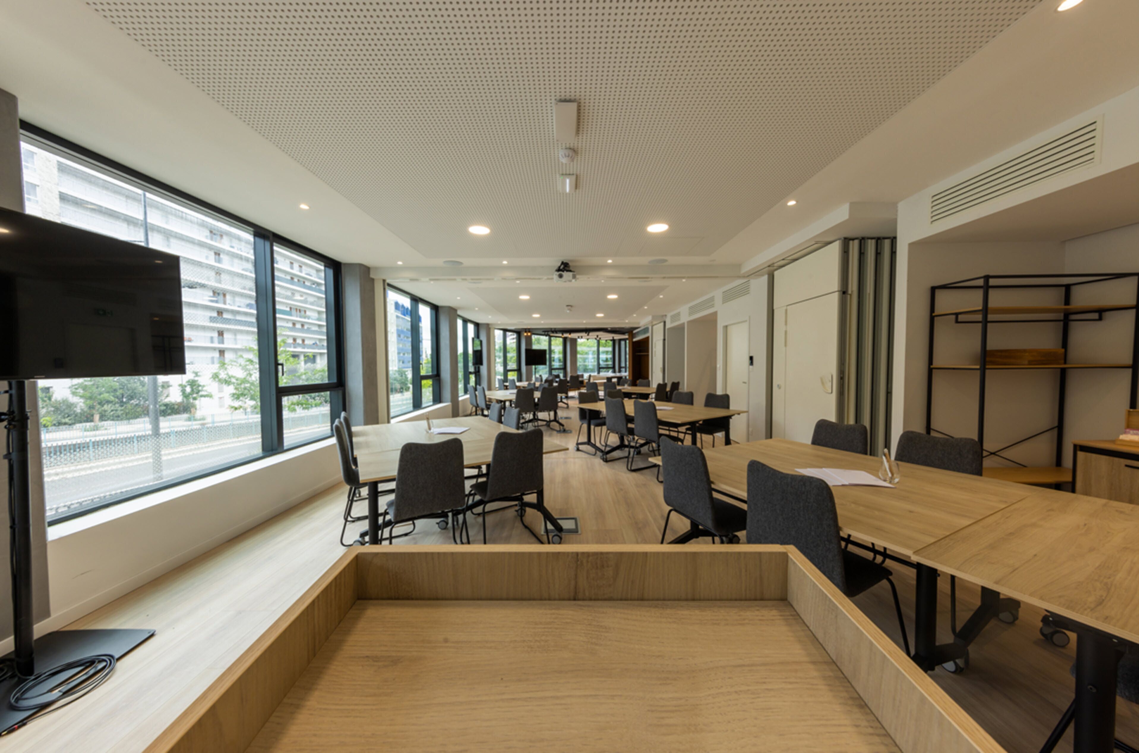 Une salle de conférence moderne dotée de grandes fenêtres, d’un téléviseur à écran plat et d’une table en bois avec des chaises.