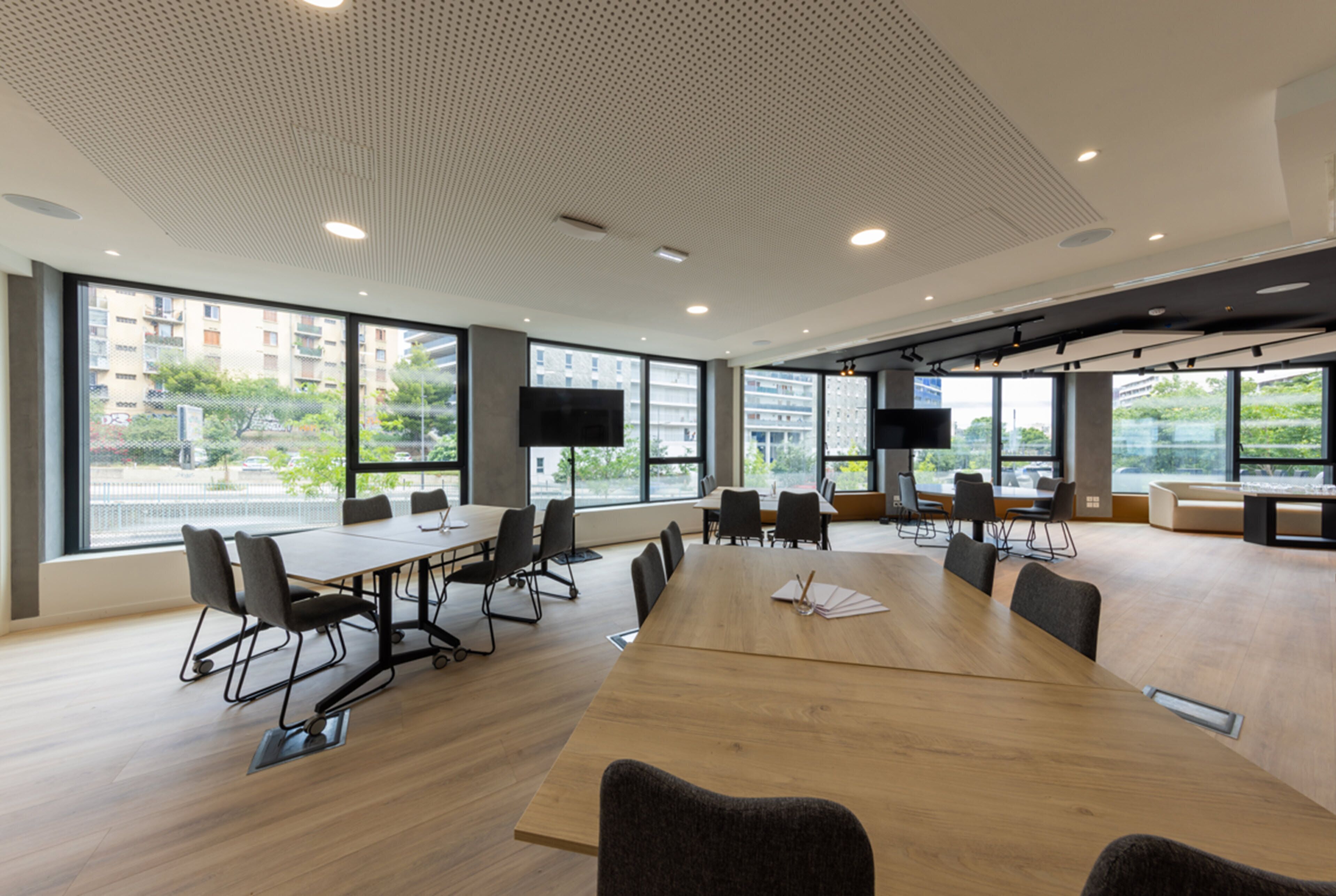 Une salle de conférence moderne, dotée d’une grande table en bois, de chaises noires et d’un téléviseur à écran plat.