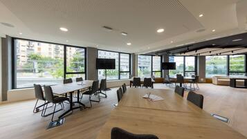 Une salle de conférence moderne, dotée d’une grande table en bois, de chaises noires et d’un téléviseur à écran plat.