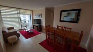 Una sala de estar con sofá, televisor, mesa de comedor con sillas y una alfombra roja.
